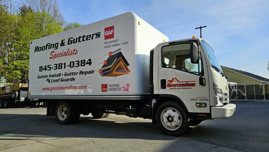 White box truck with Gonzales Roofing & Gutters branding, parked outdoors. The side panel advertises roofing and gutter services with contact information and a GAF logo.